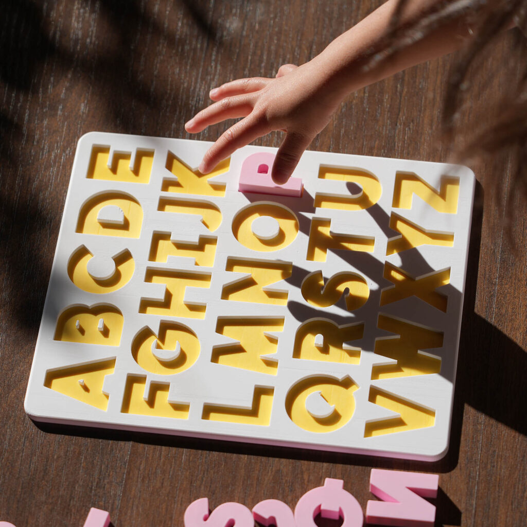 A white and yellow puzzle board, showing the English alphabet with pink capital letters