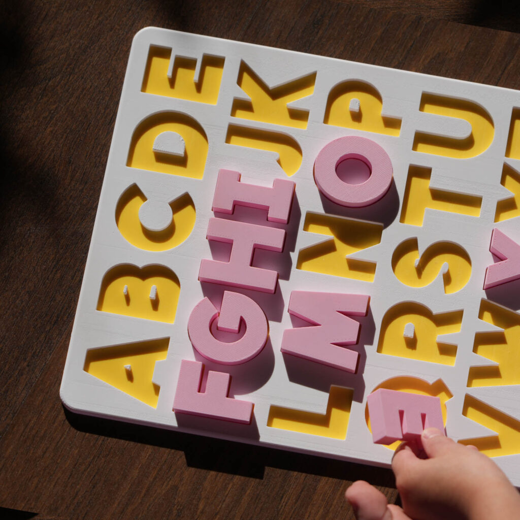 A white and yellow puzzle board, showing the English alphabet with pink capital letters