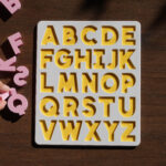 A white and yellow puzzle board, showing the English alphabet with pink capital letters