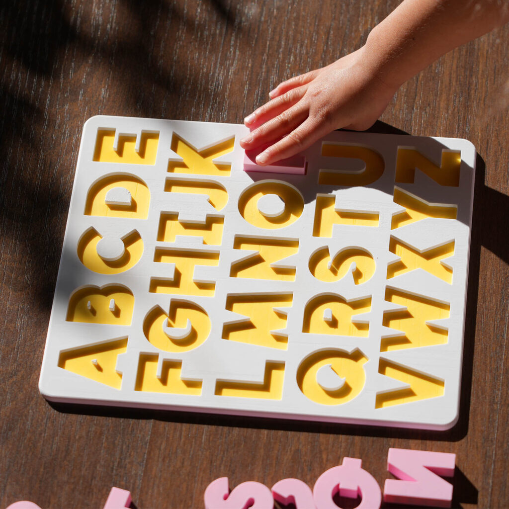 A white and yellow puzzle board, showing the English alphabet with pink capital letters
